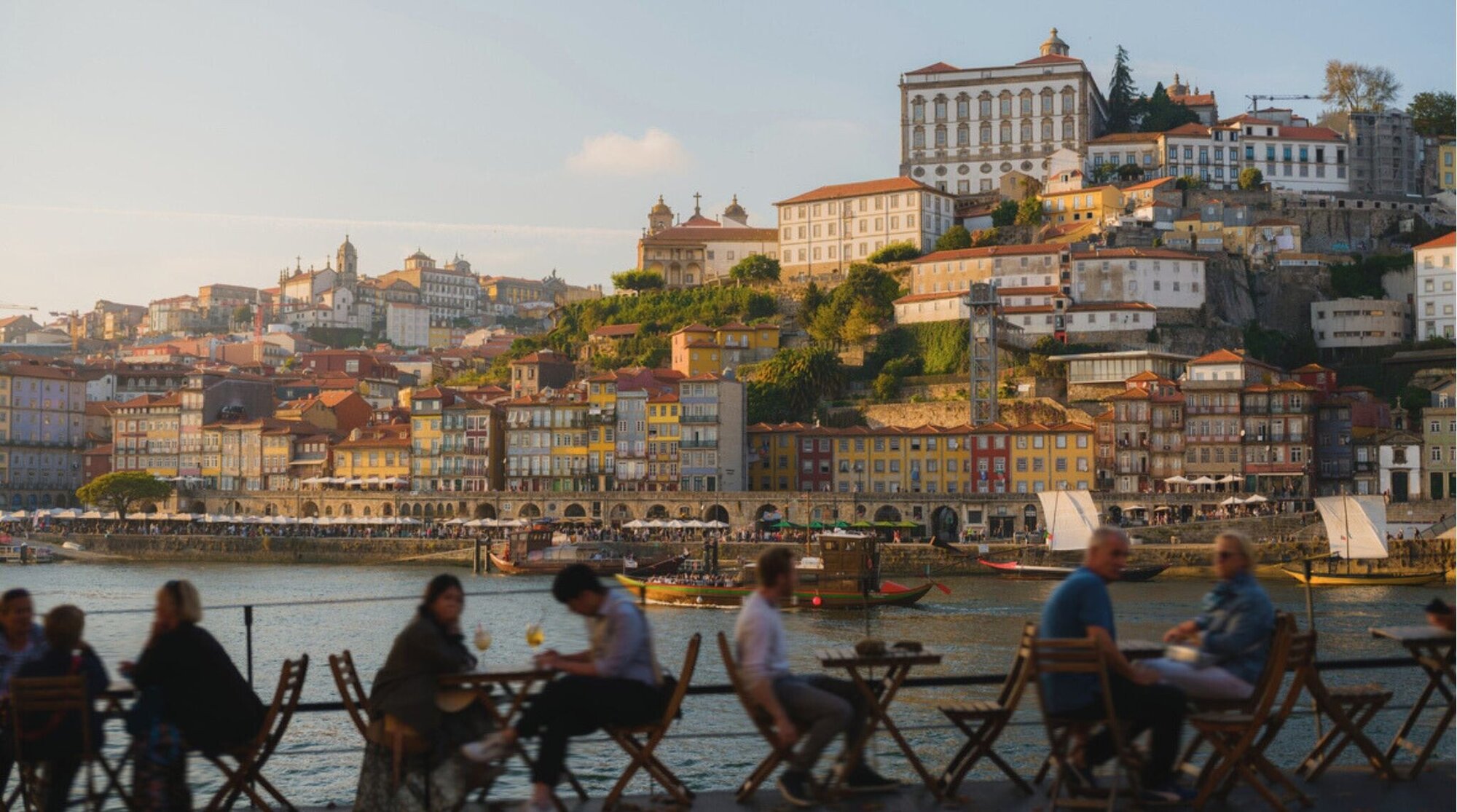 Multidão no terraço de um restaurante, apreciando o pôr do sol sobre a cidade do Porto, em Portugal.