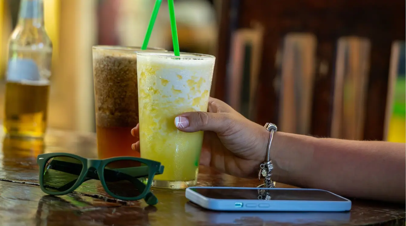 Femme tenant un jus de fruits tropicaux pendant ses vacances au Costa Rica avec son téléphone posé juste à côté. 