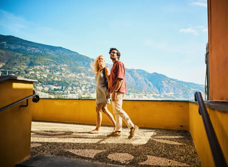 Pareja joven caminando por un callejón con vistas al mar en Mentón, Francia, conectados con eSIM regional para viajes en Europa