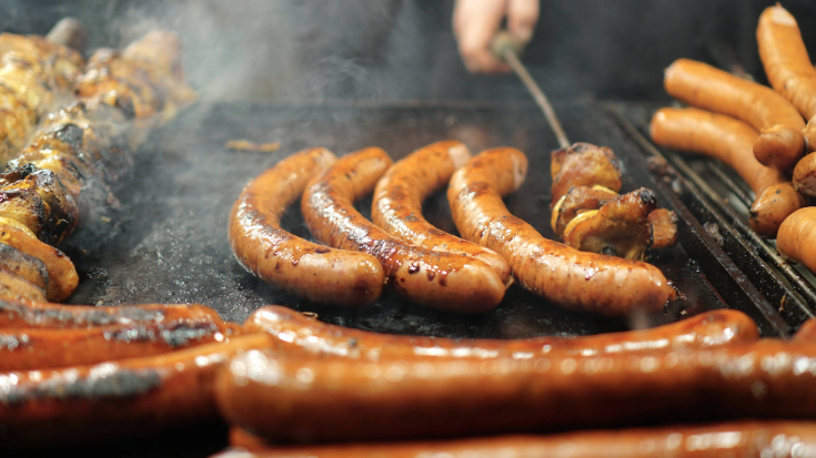 A close-up image of someone frying bratwurst and other meats on sticks at a German themed Christmas market, to illustrate a blog post entitled The Best Christmas markets in the UK for 2024.