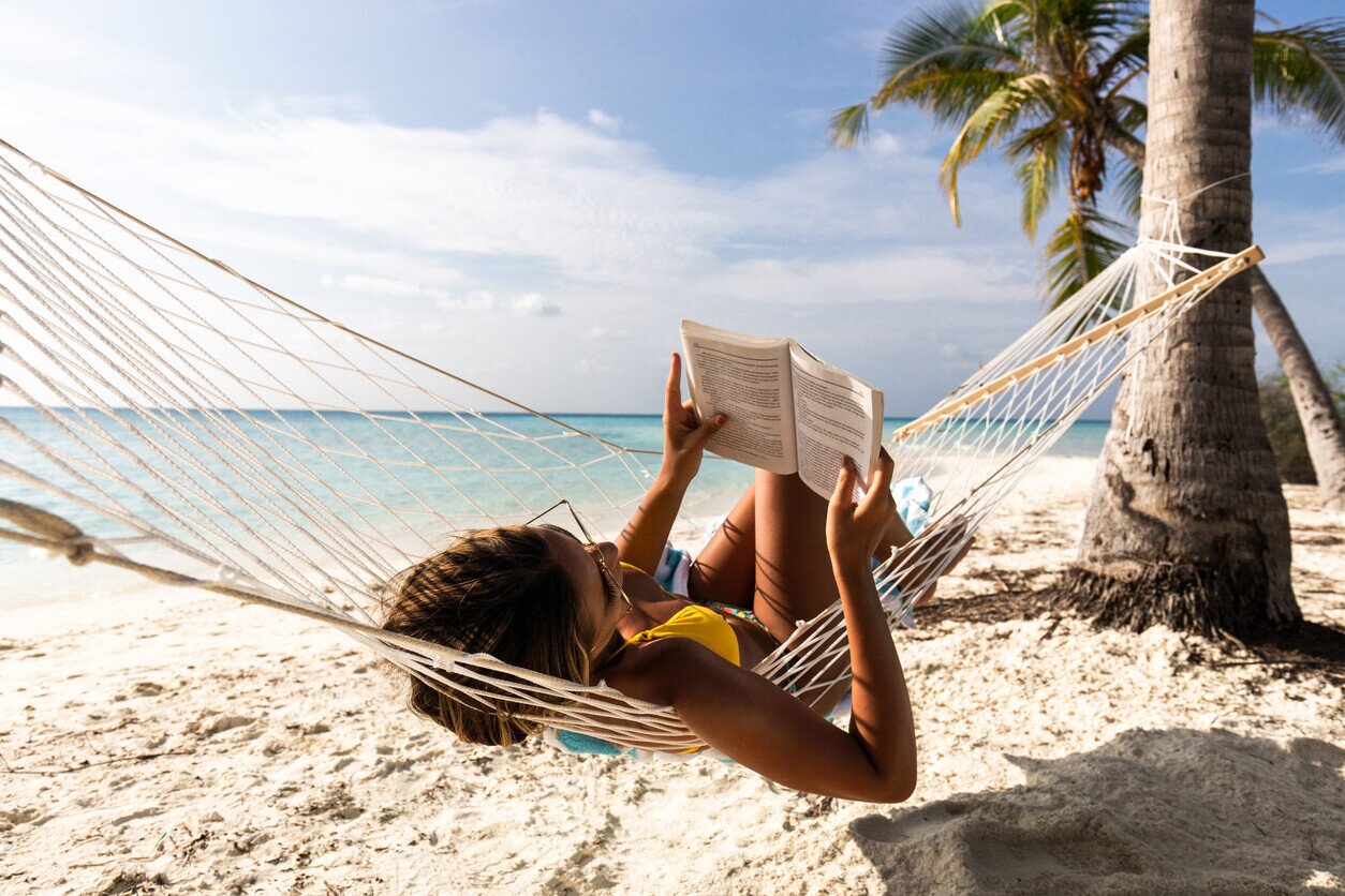 Donna rilassata che legge un libro sull'amaca sulla spiaggia.