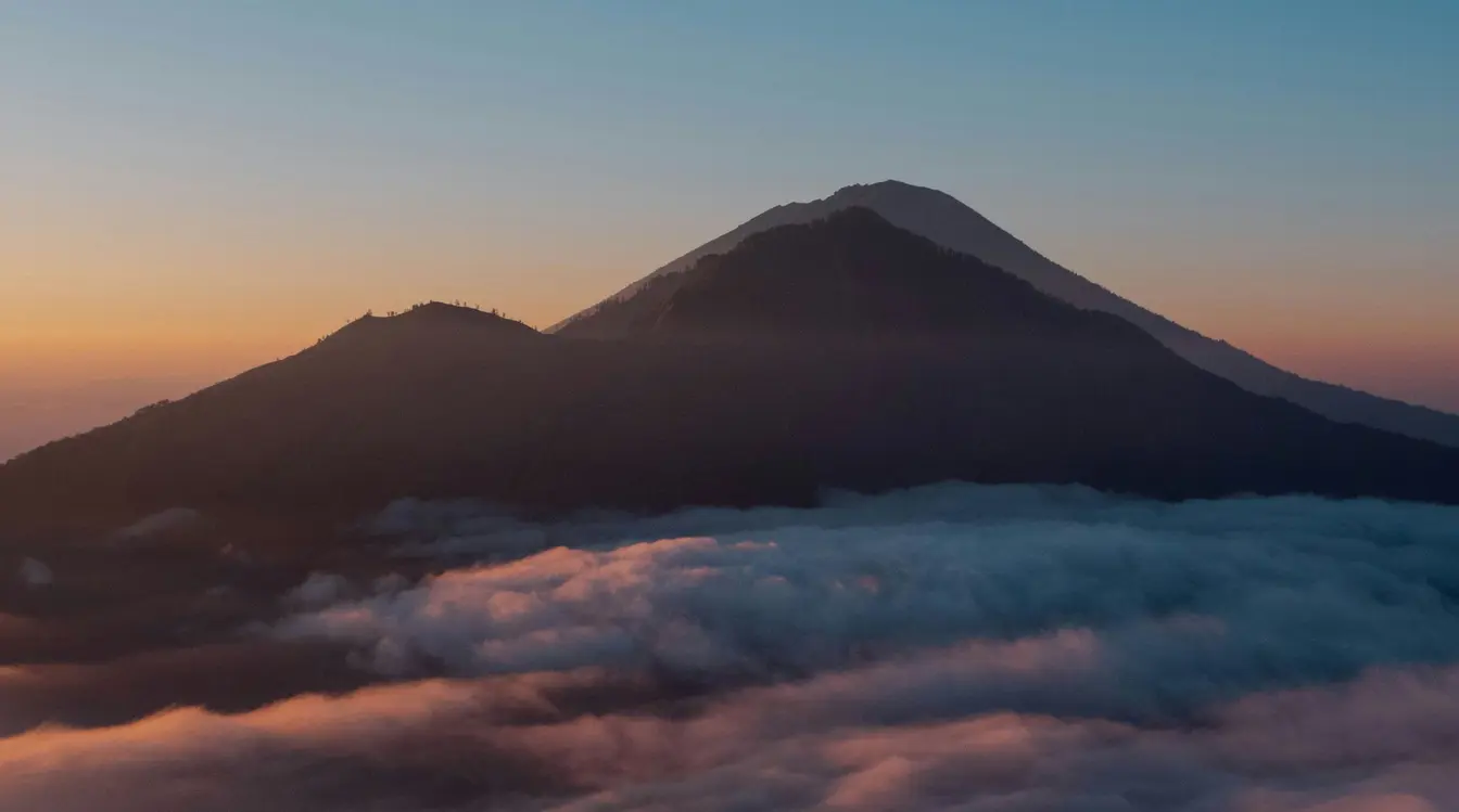 Sunrise view from Mount Batur with volcanic peaks rising above a thick sea of clouds in soft morning light.