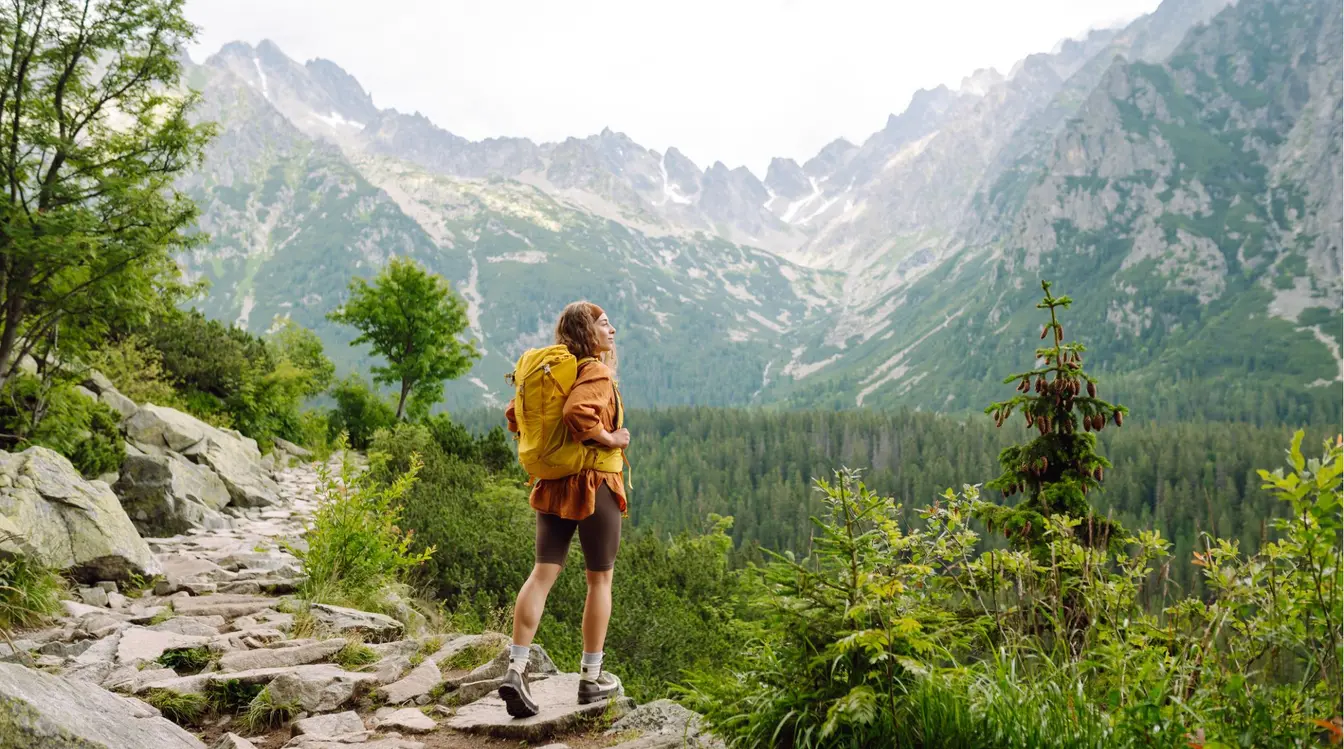  Femme seule en randonnée avec un sac à dos jaune admirant un paysage de montagne.
