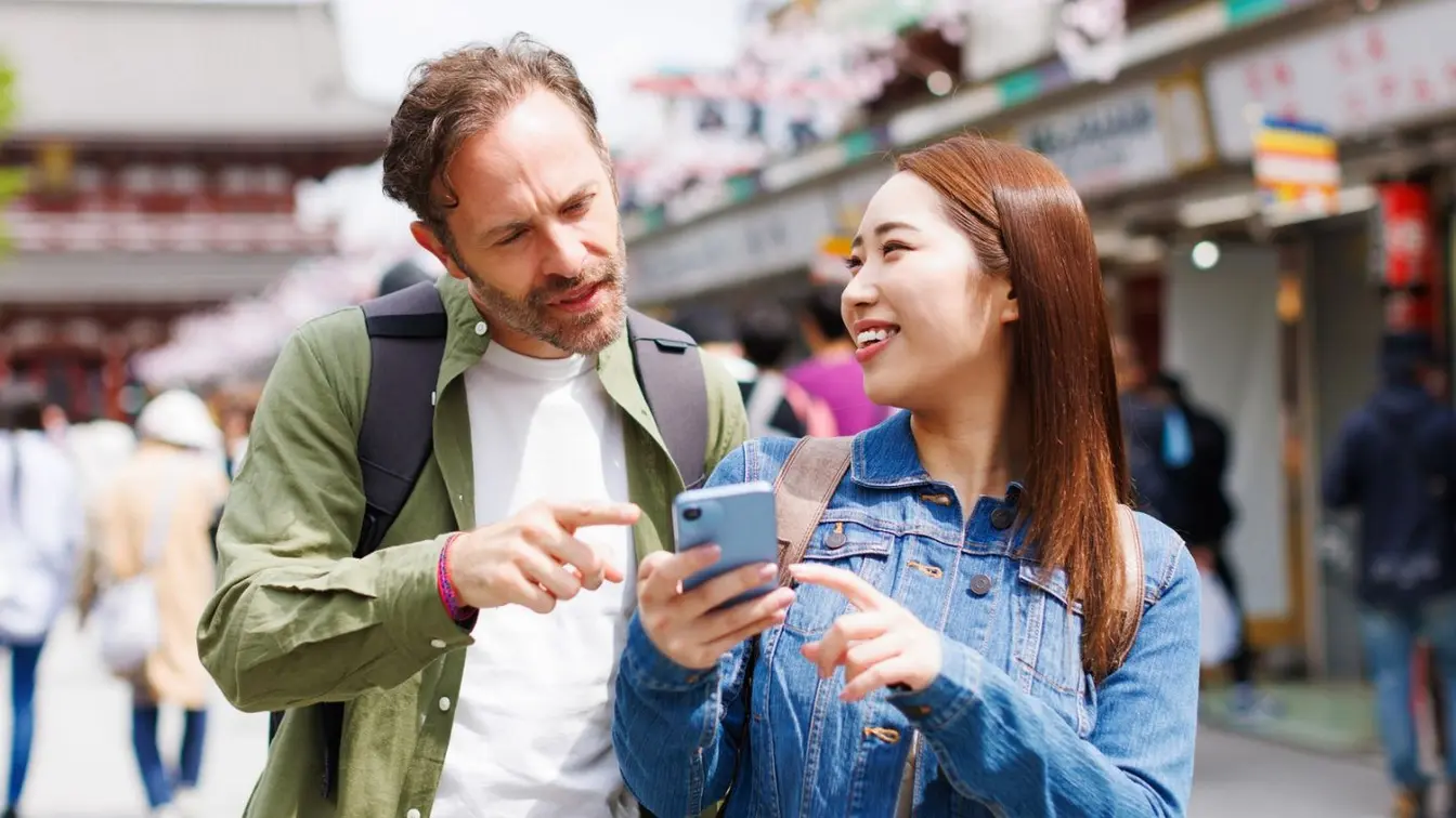A male and female couple looking at a smartphone on a street in Japan.