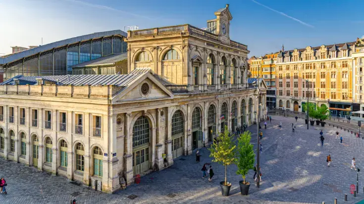 The sand-coloured historic, ornate facade of Gare de Lille Flandres train station in France, a hub for sustainable train travel.