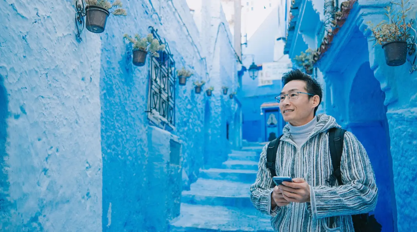 View of a man holding a phone in a blue-walled street in Chefchaouen, Morocco.