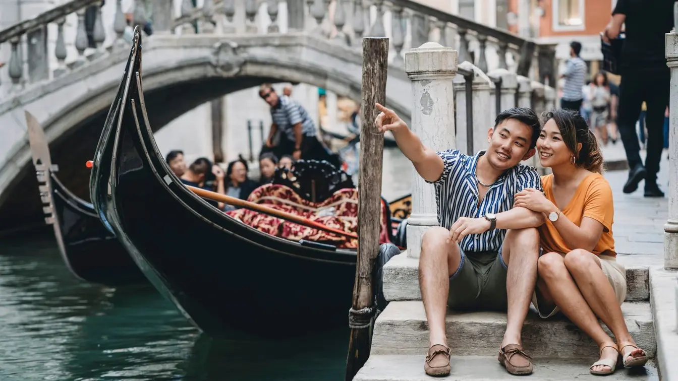 Ein Paar sitzt bei einem romantischen Urlaub in Venedig am Kanal