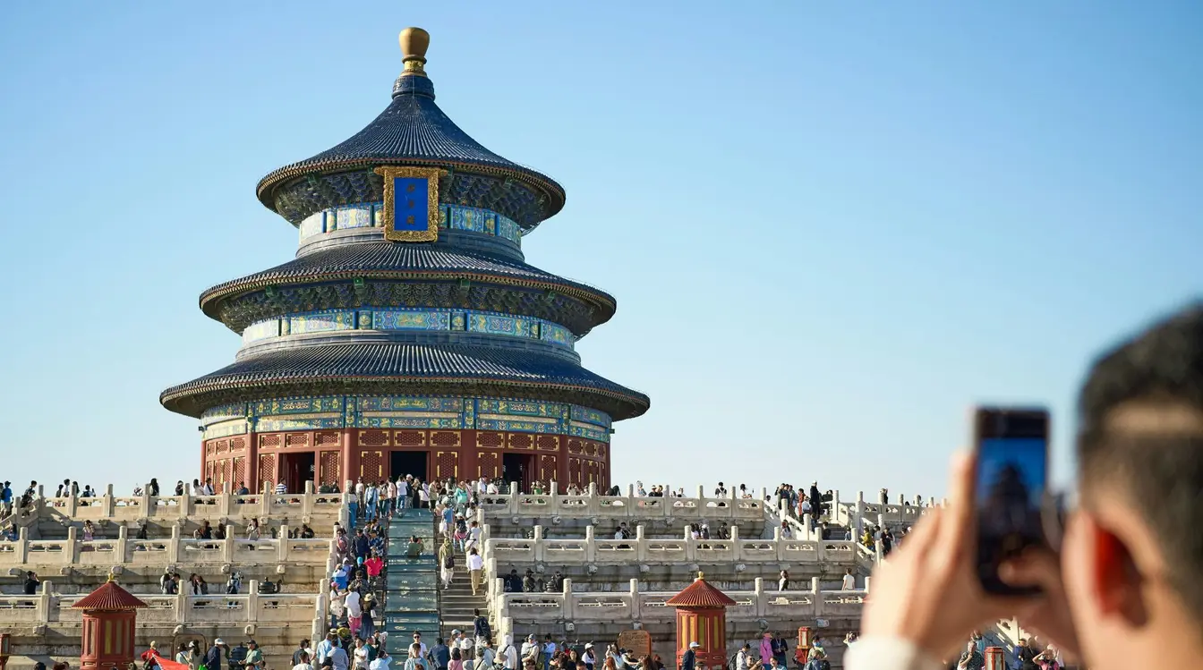 A tourist holding up a mobile phone to take a photo of the Temple of Heaven in Beijing, China.