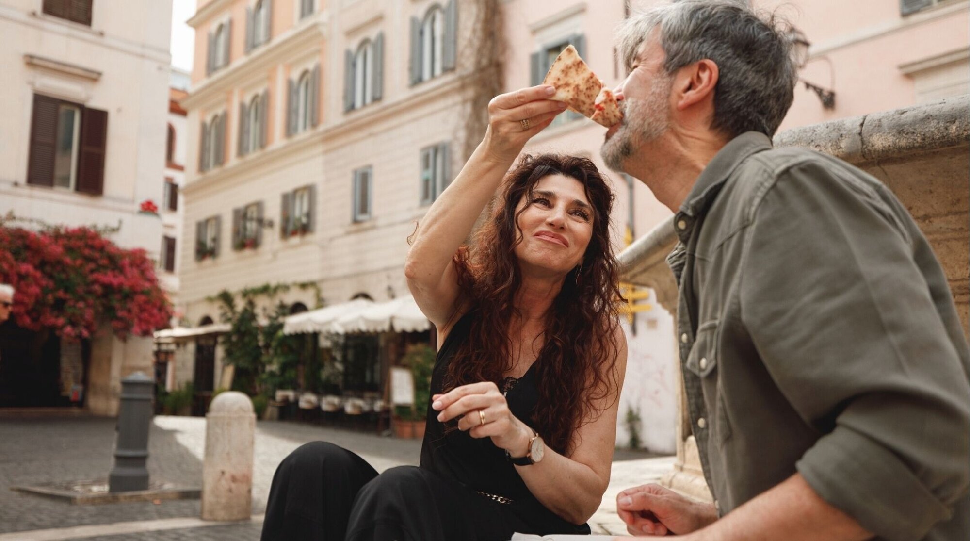 Pareja mayor compartiendo pizza en una plaza de Roma, Italia.