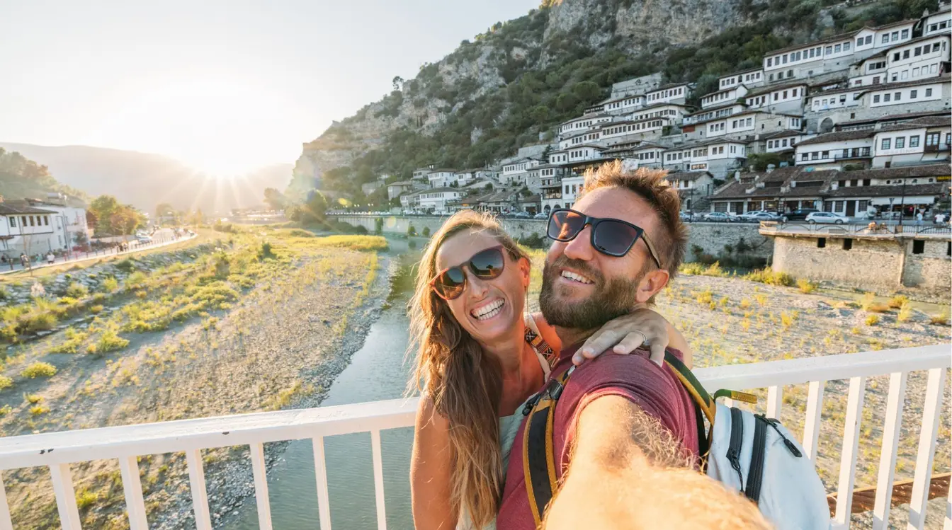 Couple heureux prenant un selfie devant un village de montagne en Albanie.