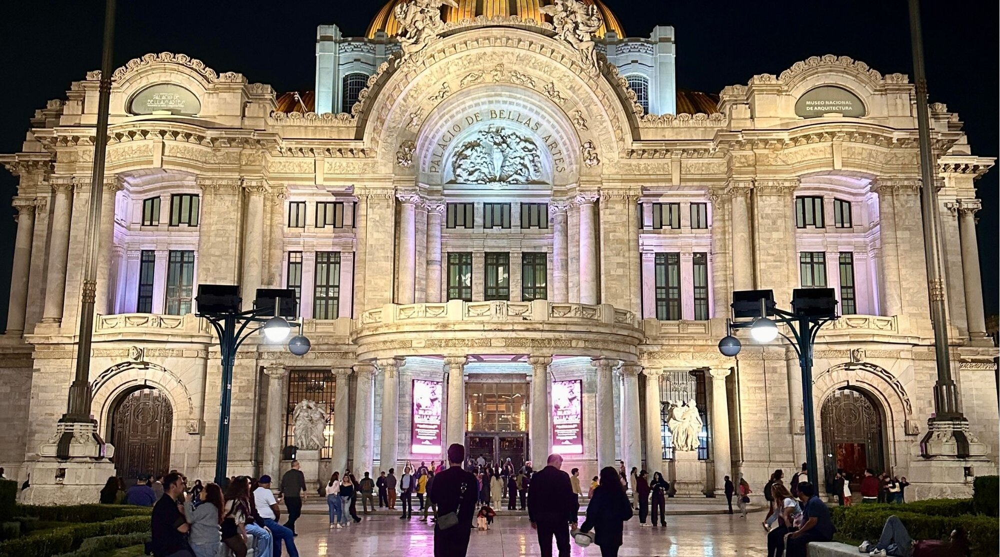 Movimentação de pedestres diante da imponente arquitetura do Palácio de Bellas Artes iluminado durante a noite