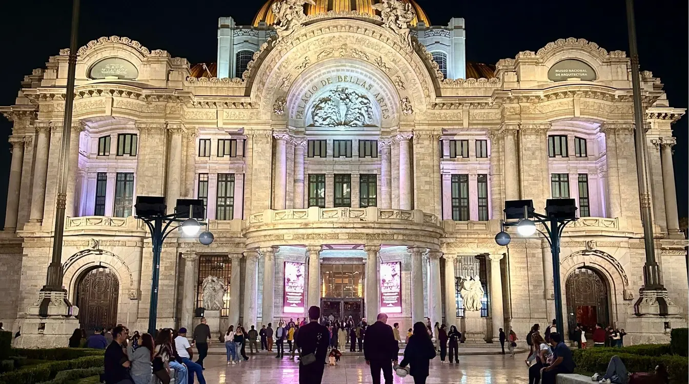 Movimentação de pedestres diante da imponente arquitetura do Palácio de Bellas Artes iluminado durante a noite