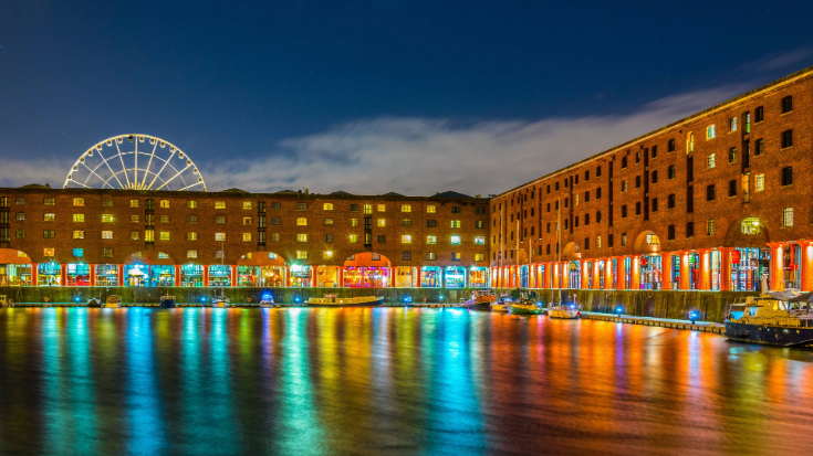 A nighttime image of Liverpool's Albert Dock, with lot s of colourful lights reflecting on the water and a ferris wheel in the background, to illustrate a blog post entitled the Best Christmas markets in the UK in 2024.