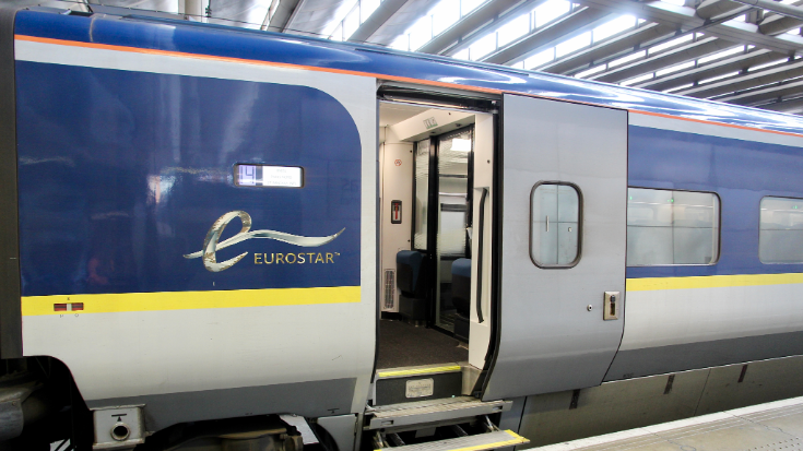 A colour image showing the side of a Eurostar train, sitting in a station and waiting for passengers to board. the Eurostar logo is shown on the side of the train. The train carriages are blue with yellow stripes running through their middle section.To illustrate a blog post entitled 'Extreme Day Trips: Eurostar Christmas Markets Edition'.