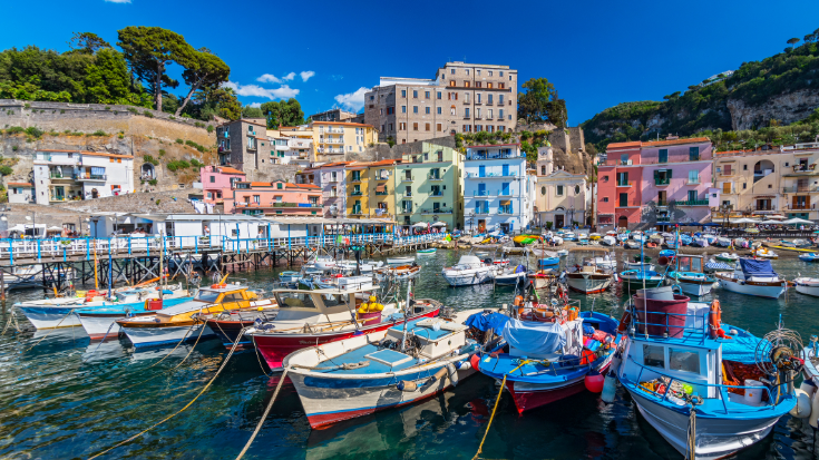 A colour photo of Sorrento, showing hotels and buildings painted in bright yellow, salmon, and white, overlooking a busy marina.
