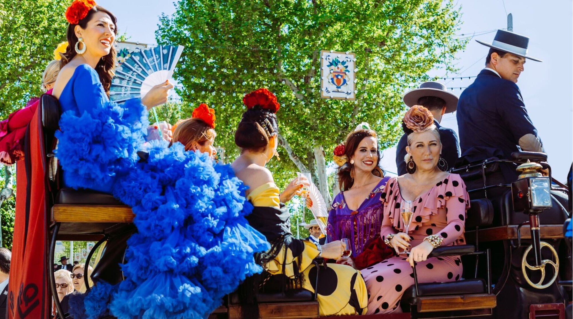 Mulheres bonitas no vestido tradicional e colorido que viajam em carruagens desenhadas cavalo na feira de abril, feira de Sevilha (Feria de Sevilla)