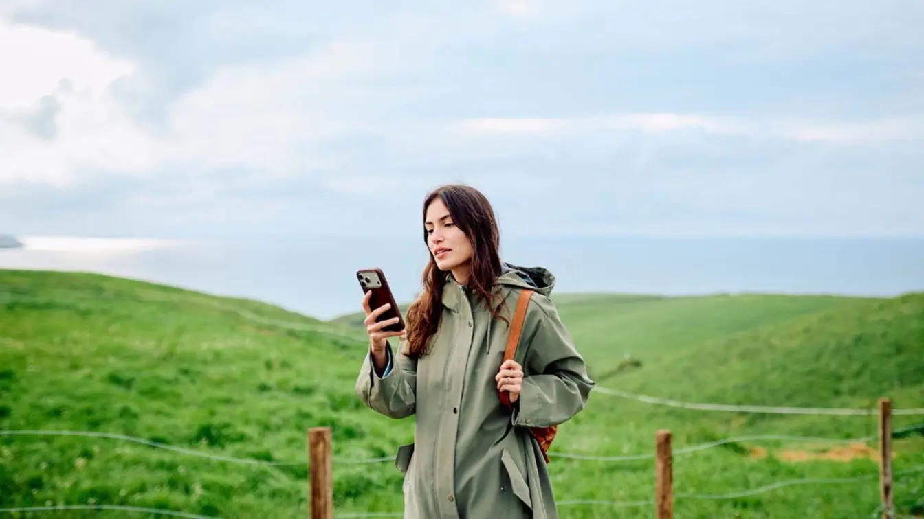 Mulher usando celular em um campo verde.