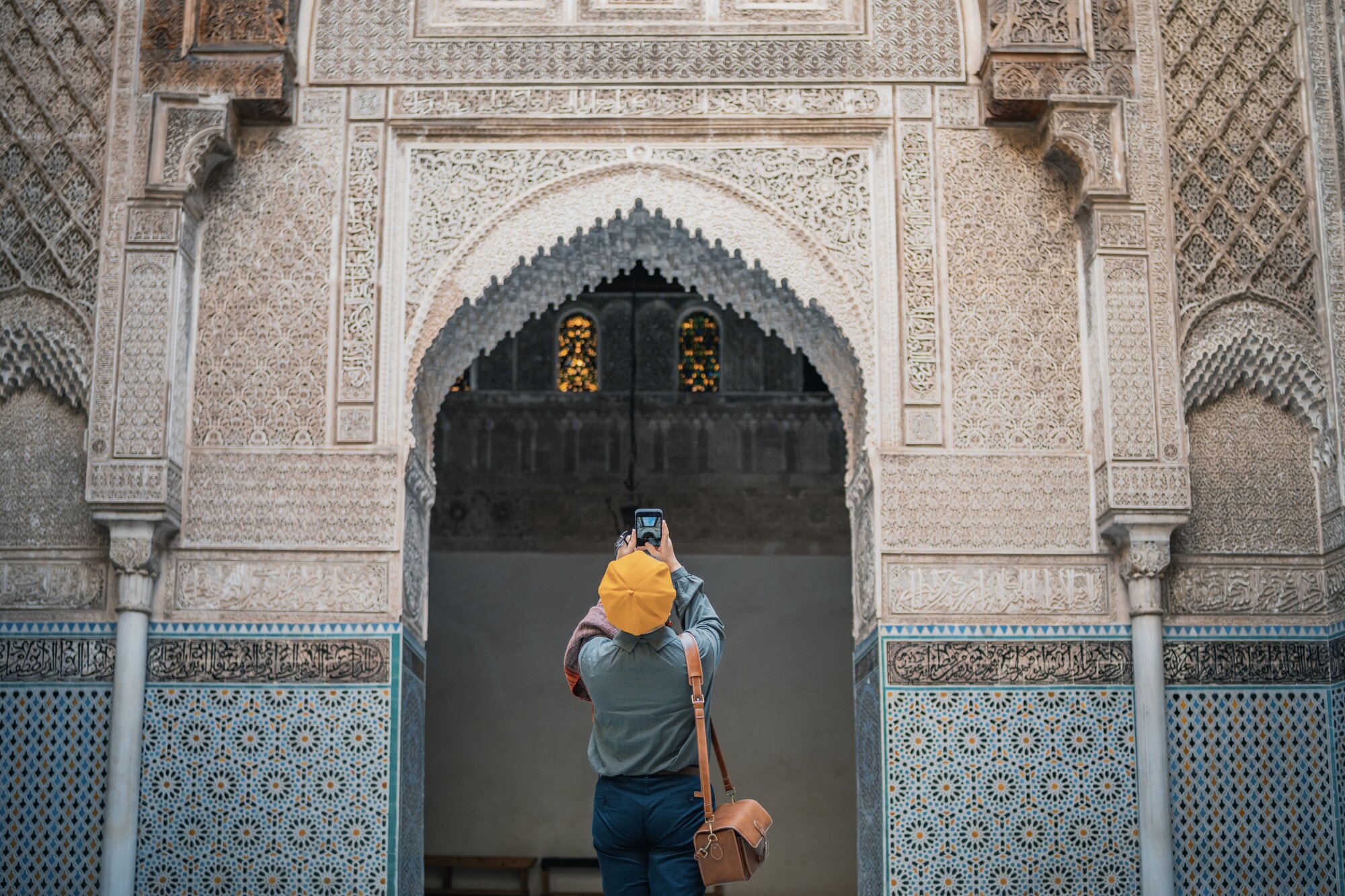 Femme de dos prenant en photo l'architecture de la Médersa Bou Inania à Fès, utilisant son smartphone connecté via une eSIM au Maroc