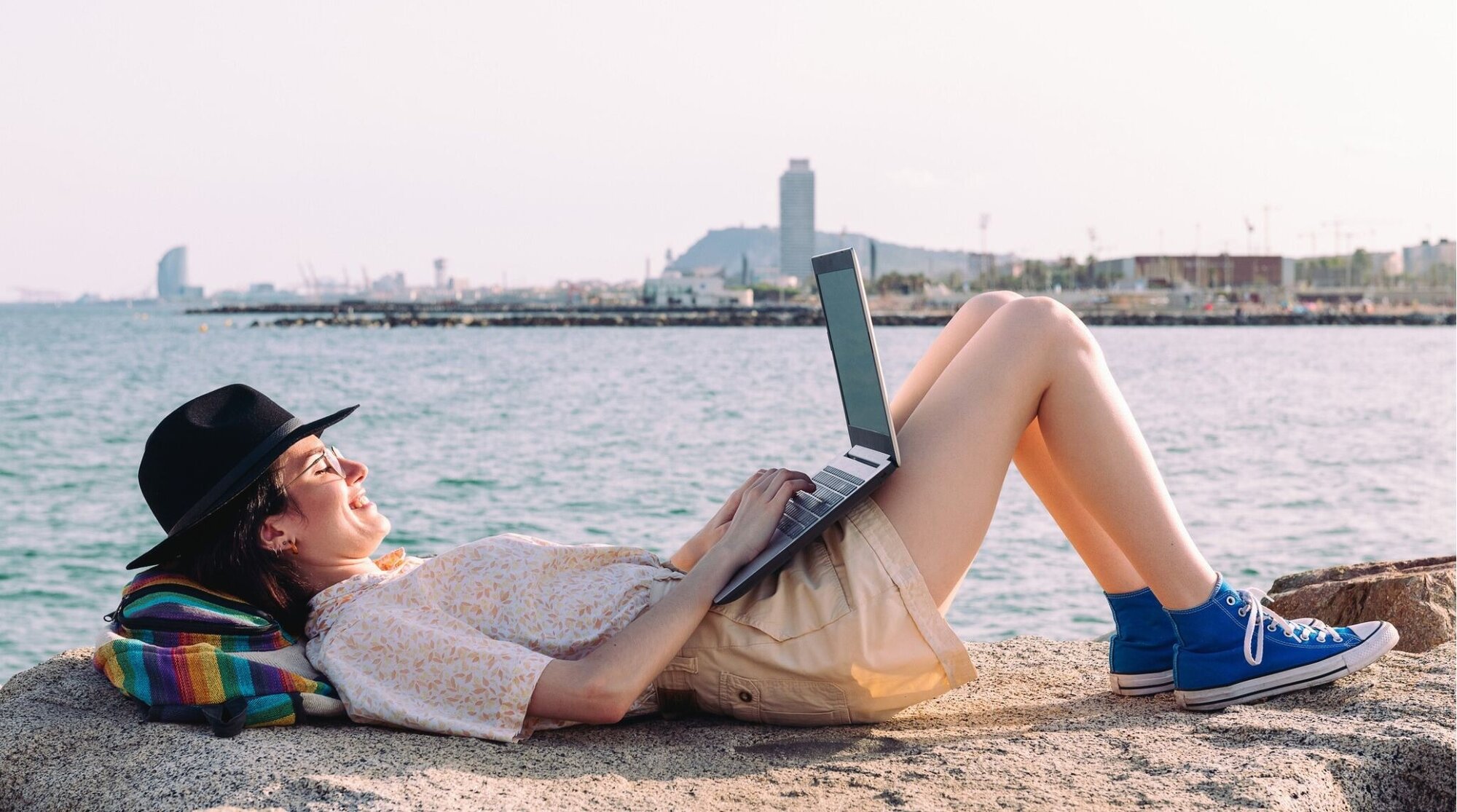 Viajera trabajando con portátil junto al mar, alternativa de internet si su móvil no es compatible con eSIM.