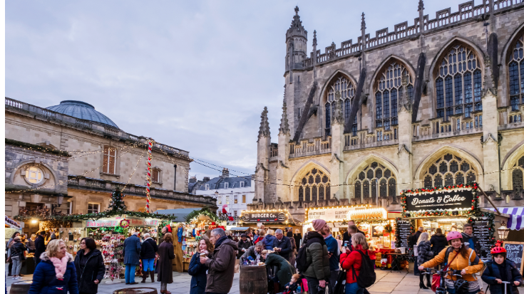 A photograph showing visitors walking around Bath Christmas Market in the UK, on Kingston Parade, at the foot of Bath Abbey. To illustrate a blog post entitled ''Extreme Day Trips - UK Christmas Markets Edition'.