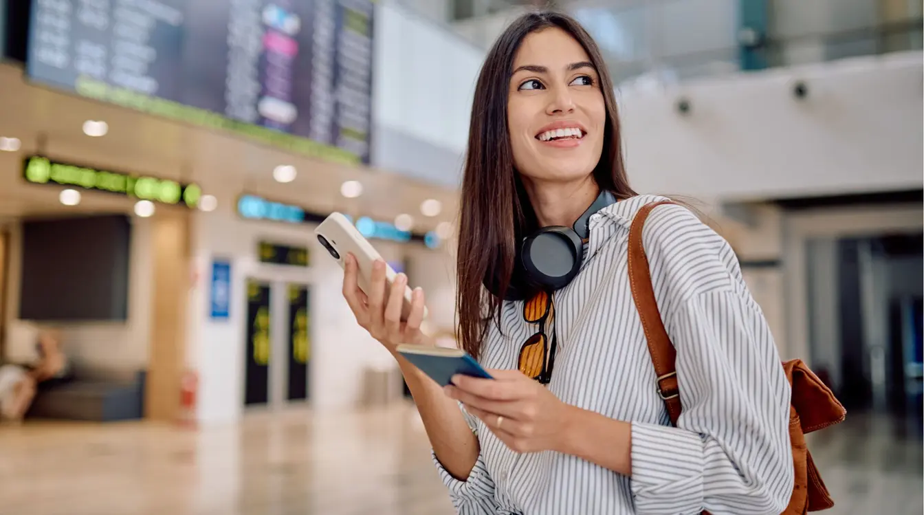 Jovem viajante usando o celular no aeroporto para conferir os dados de sua passagem aérea. 