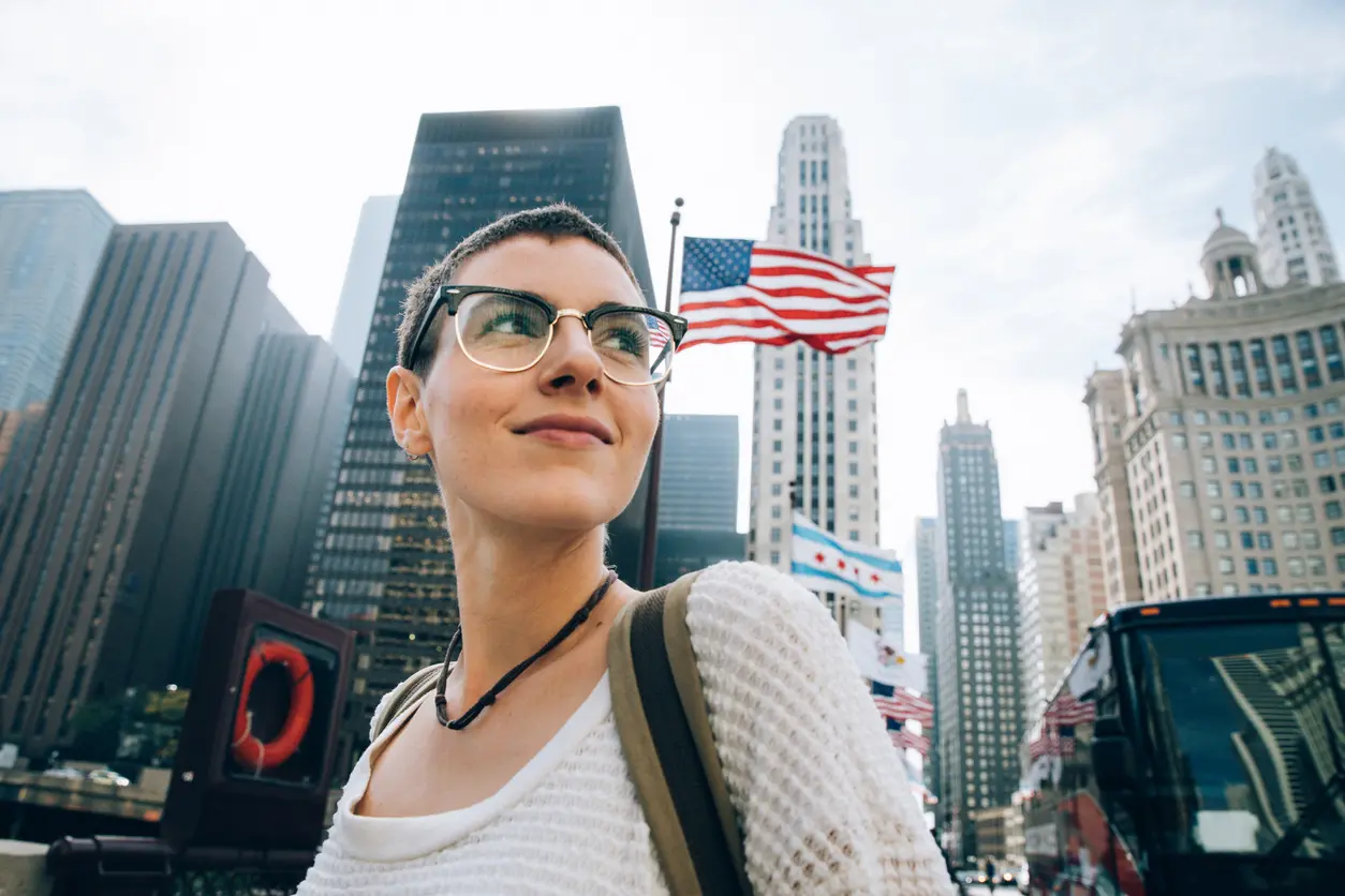 Viajera en el centro de Nueva York, Estados Unidos, con edificios altos y una bandera estadounidense al fondo.