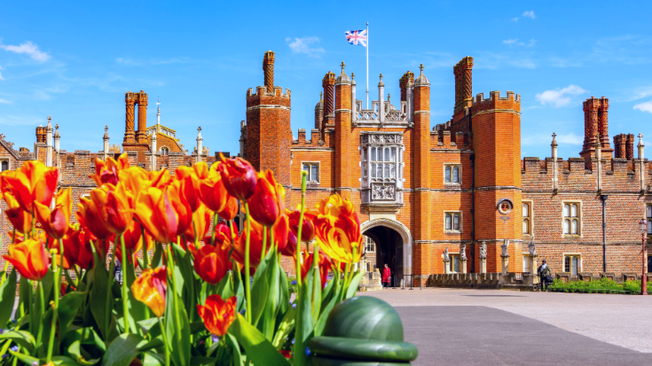 The redbrick Tudor Gatehouse at Hampton Court Palace, with a guard and Union Jack flag in the background and tulips in the foreground.