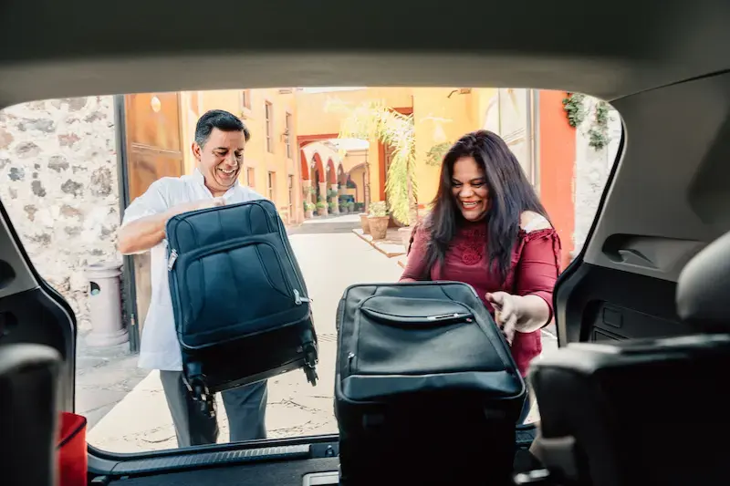 Pareja descargando maletas del auto al llegar a su alojamiento después de cruzar la frontera con datos activos. 