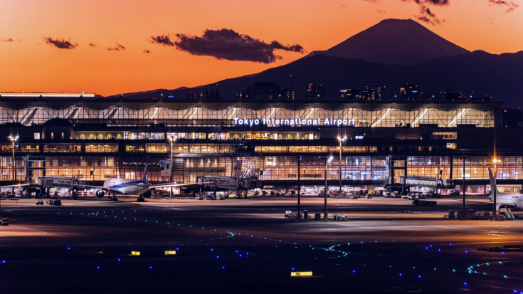 Tokyo International Airport lit up at sunset with Mount Fuji silhouetted in the background — the gateway for Tokyo Game Show 2025 visitors, where using the best eSIM for Japan makes staying connected easy as soon as you land.