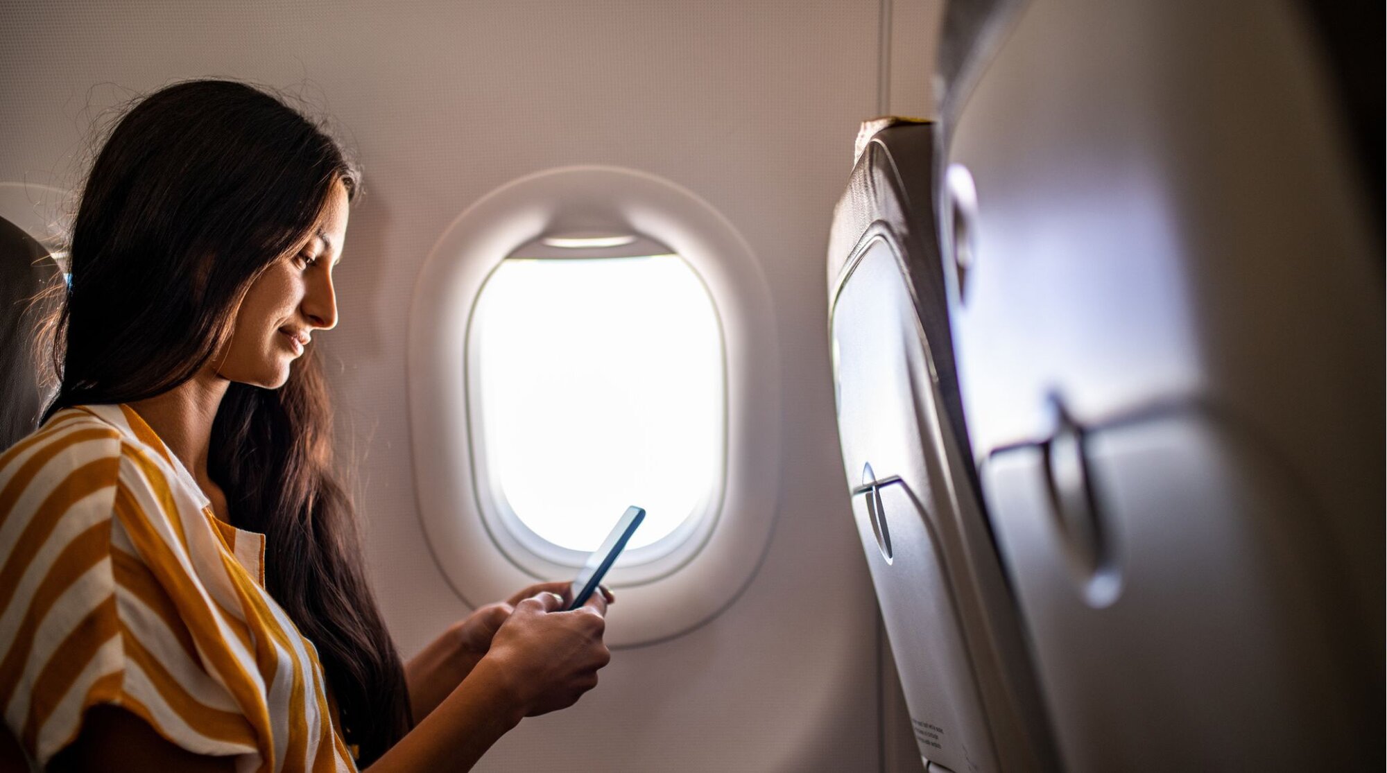 Femme voyageant en avion et utilisant son téléphone avant un départ à l’étranger.
