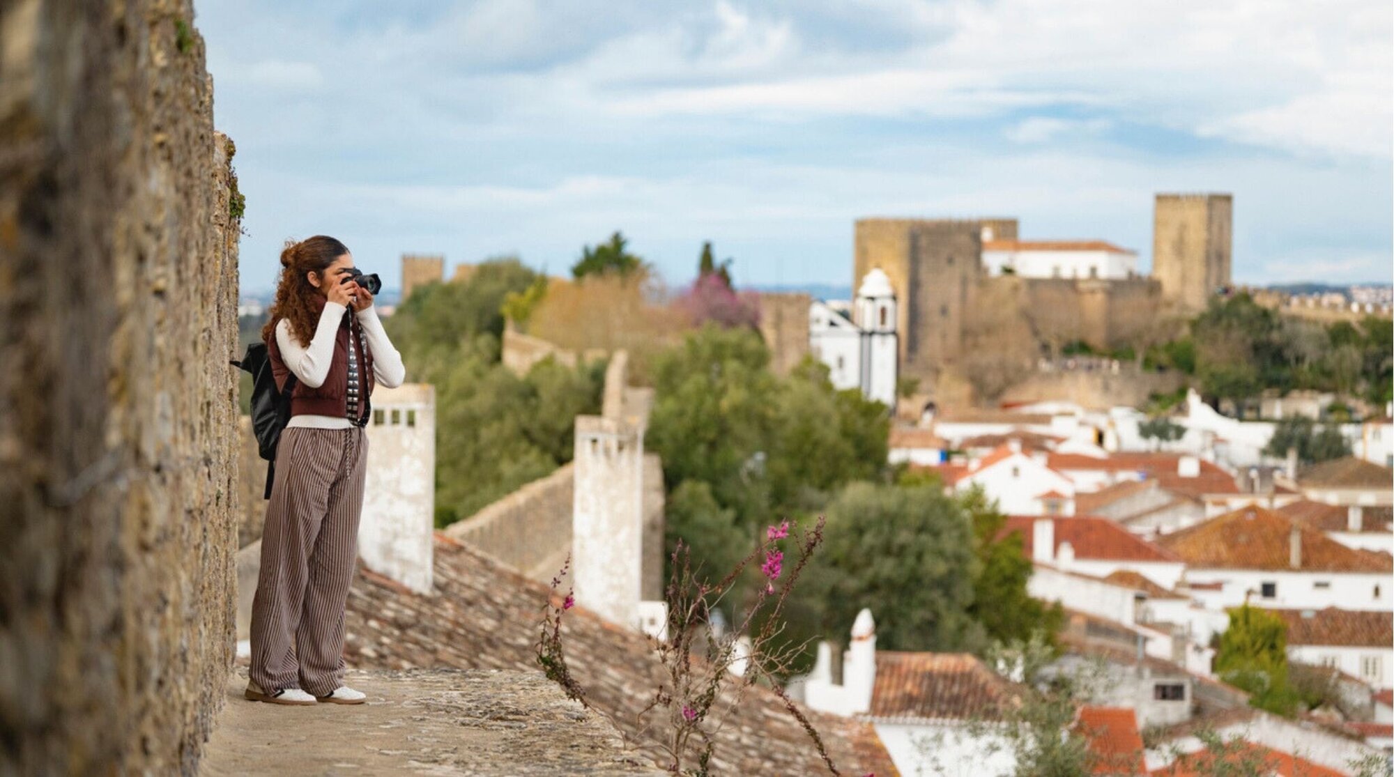 Jovem caminhando pelas muralhas de Óbidos e fotografando a paisagem.