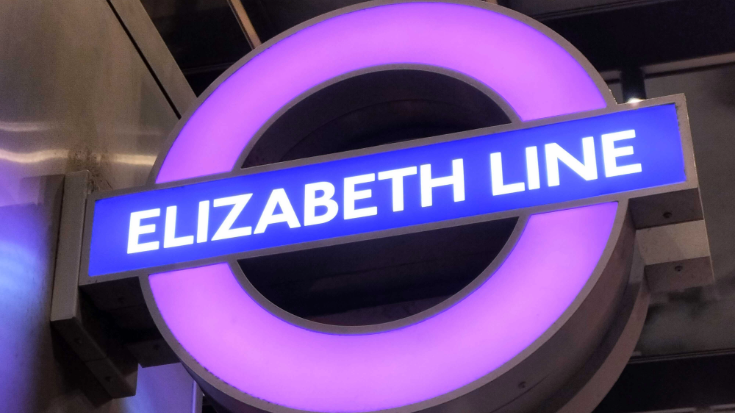 A close up of an Elizabeth Line Tube sign, with its purple circle and horizontal blue rectangle.