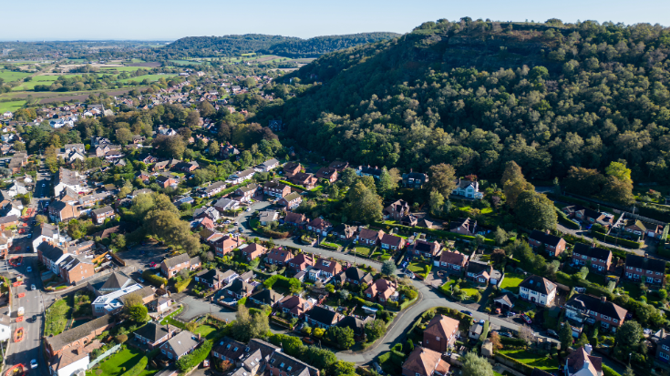 An aerial view of the village of Helsby, showing rolling green hills and the Cheshire countryside in the background.
