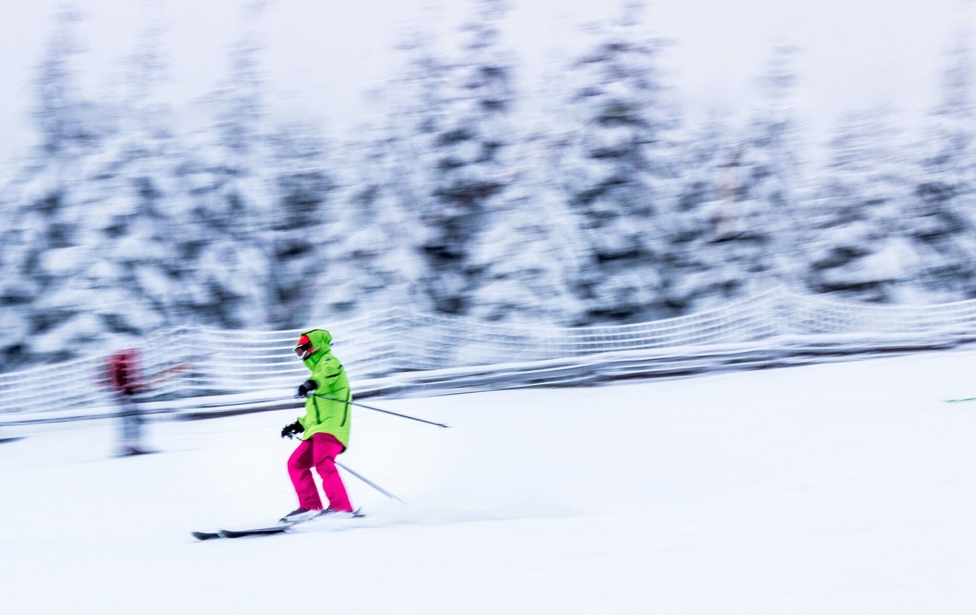 Person on a ski trip wearing green and pink going down a hill