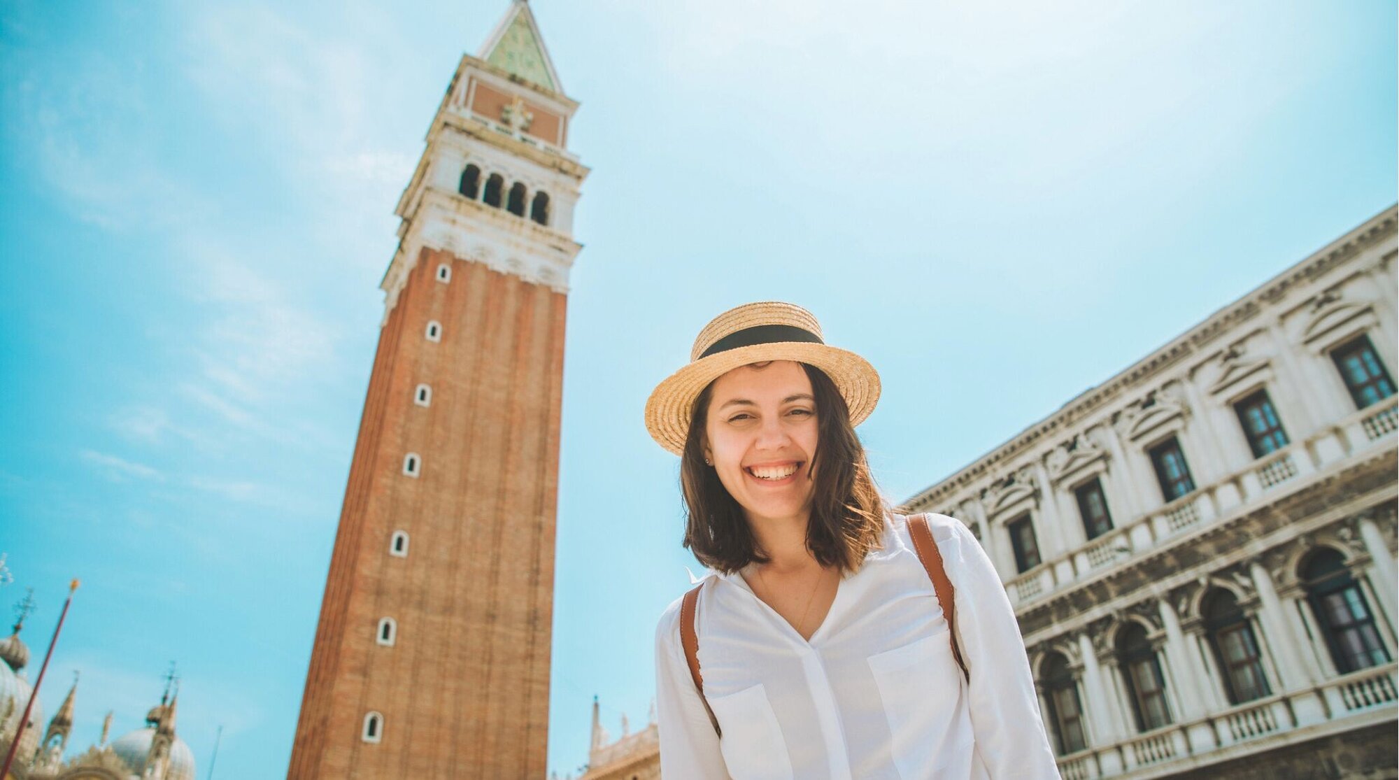 Mulher adulta sorrindo para foto com Torre do Campanário no fundo.