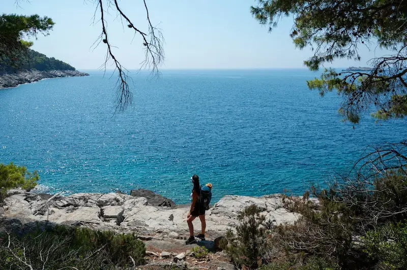 Ragazza backpacker guarda il mare dalla scogliera in estate in una delle mete economiche agosto 2026