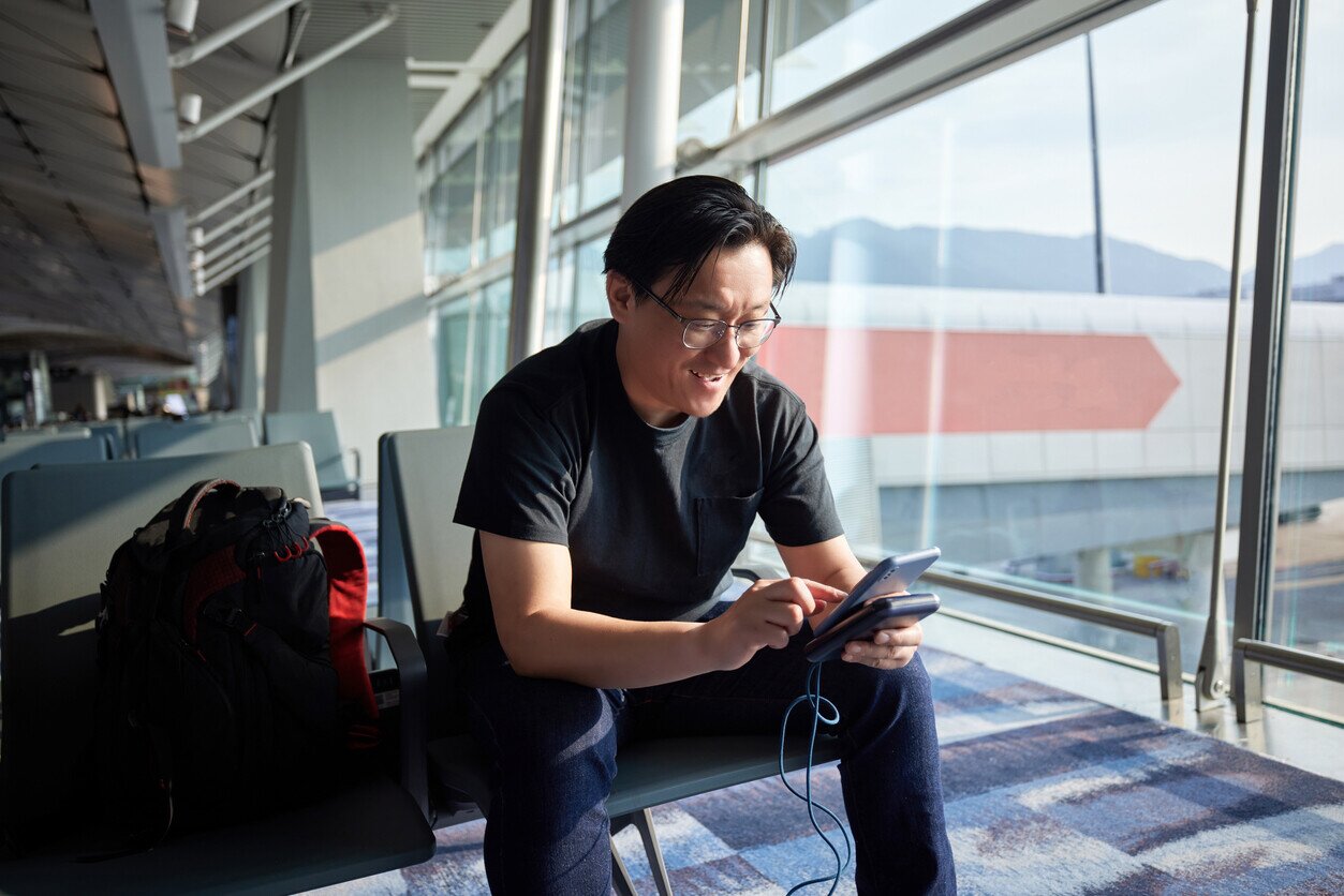 A man sitting at the airport charging his phone with a portable charger