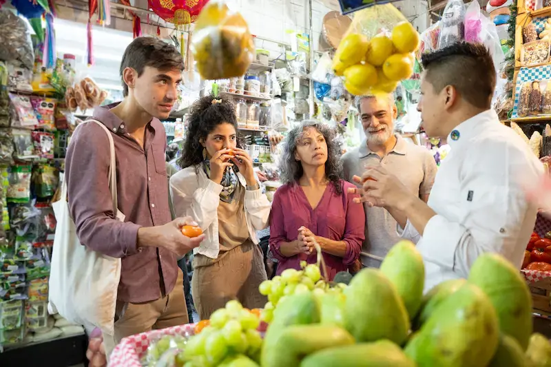 Grupo de turistas en un mercado mexicano durante una visita guiada gastronómica, con frutas en primer plano.
