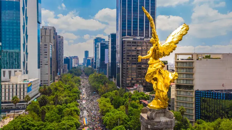 Ángel de la Independencia en Ciudad de México con edificios modernos y una multitud sobre Paseo de la Reforma.