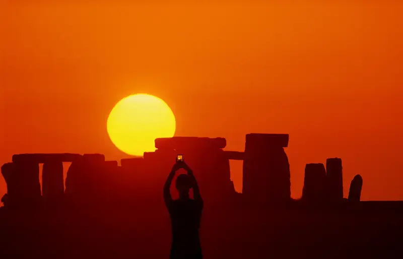 Alba Stonehenge con persona che fotografa sole e cielo rossi