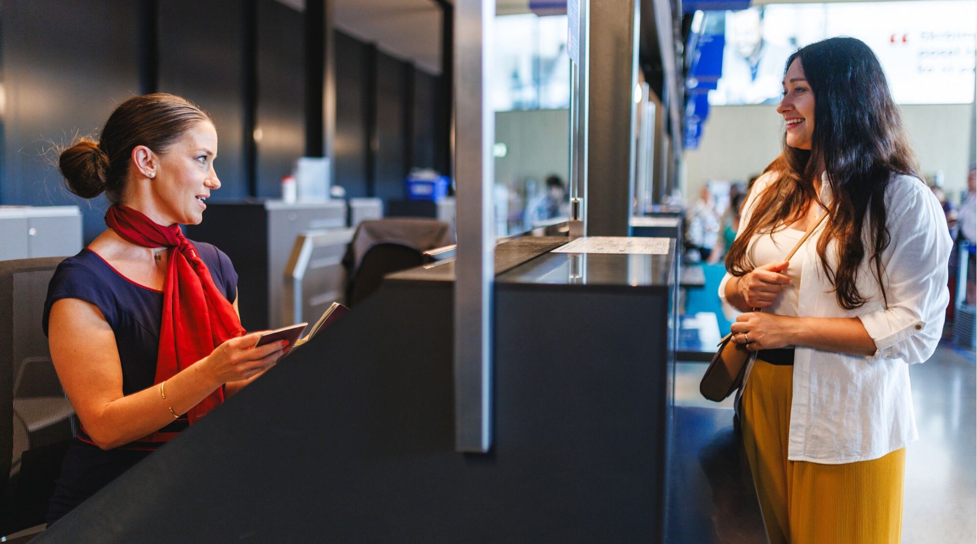 Funcionária de aeroporto verificando passaporte de viajante no balcão de check-in.