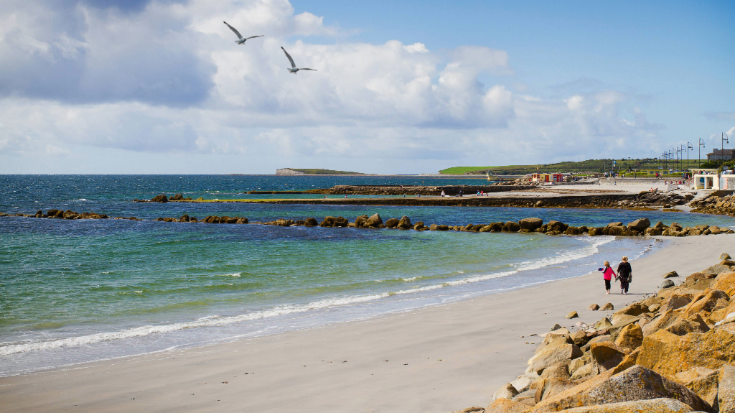 An empty white sand beach against a bright blue sky on the West coast of Ireland, at Salthill, Galway.