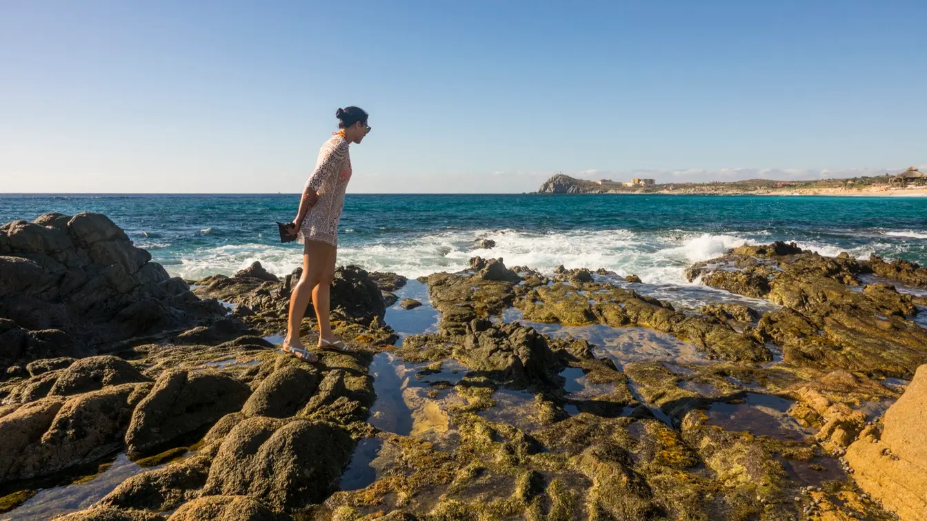 Mujer caminando sobre formaciones rocosas junto al mar en Los Cabos