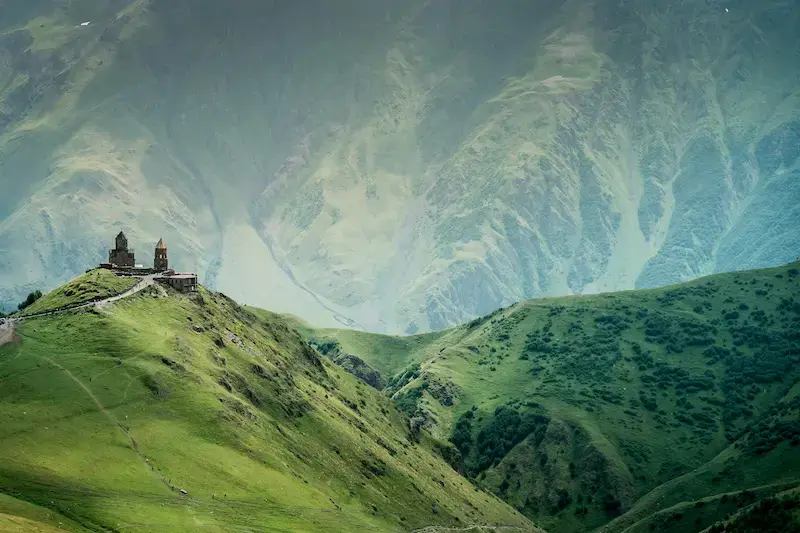 Vista della Gergeti Trinity Church in Georgia con sfondo di montagne verdi, meta di vacanze low cost agosto