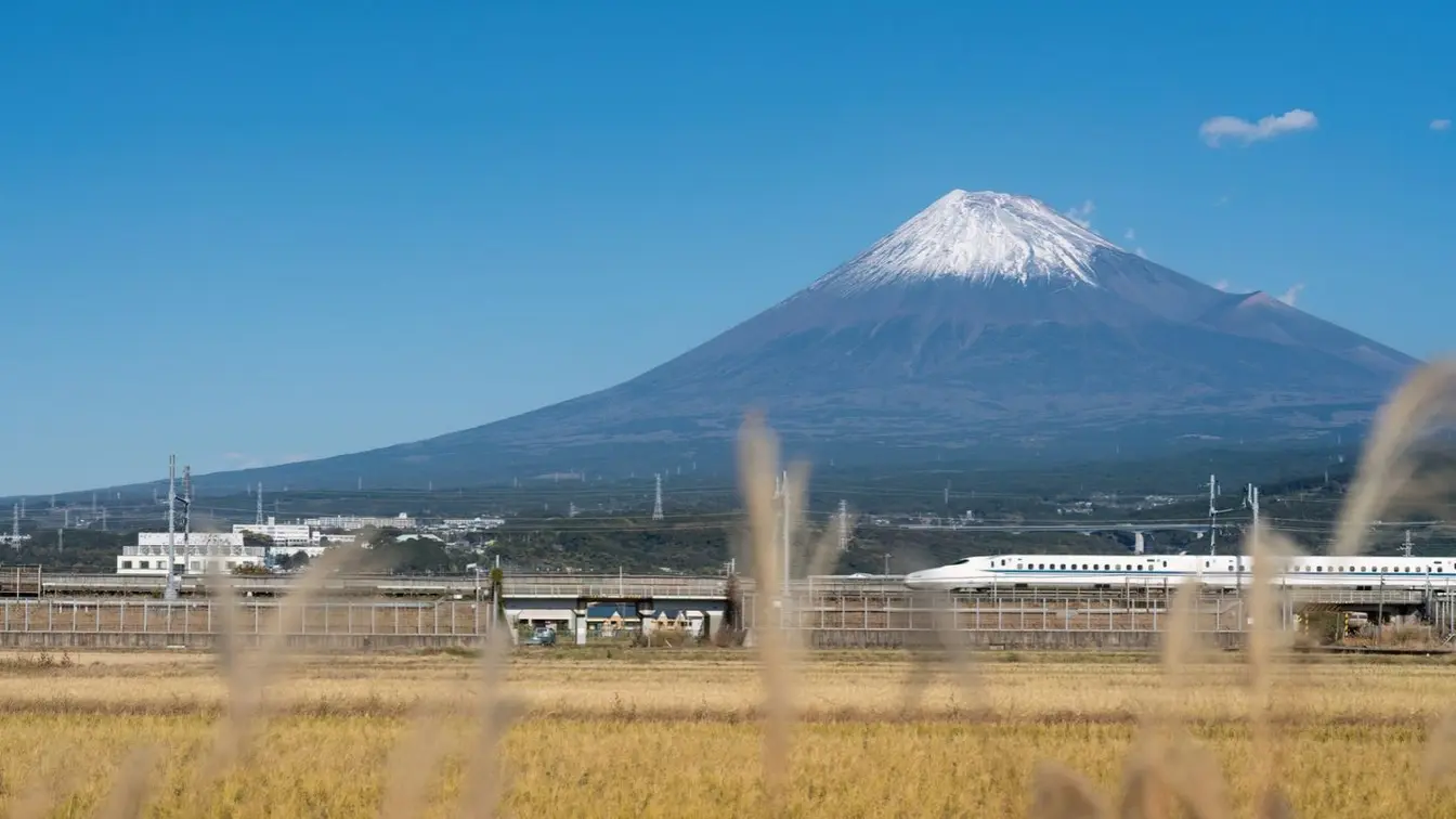 View of a Shinkansen bullet train passing in front of Mount Fuji.