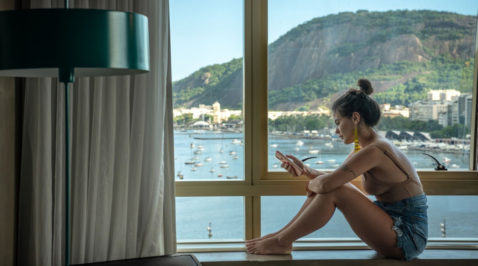 touriste utilisant son téléphone près d’une fenêtre donnant sur la baie de Guanabara - Rio de Janeiro, Brésil
