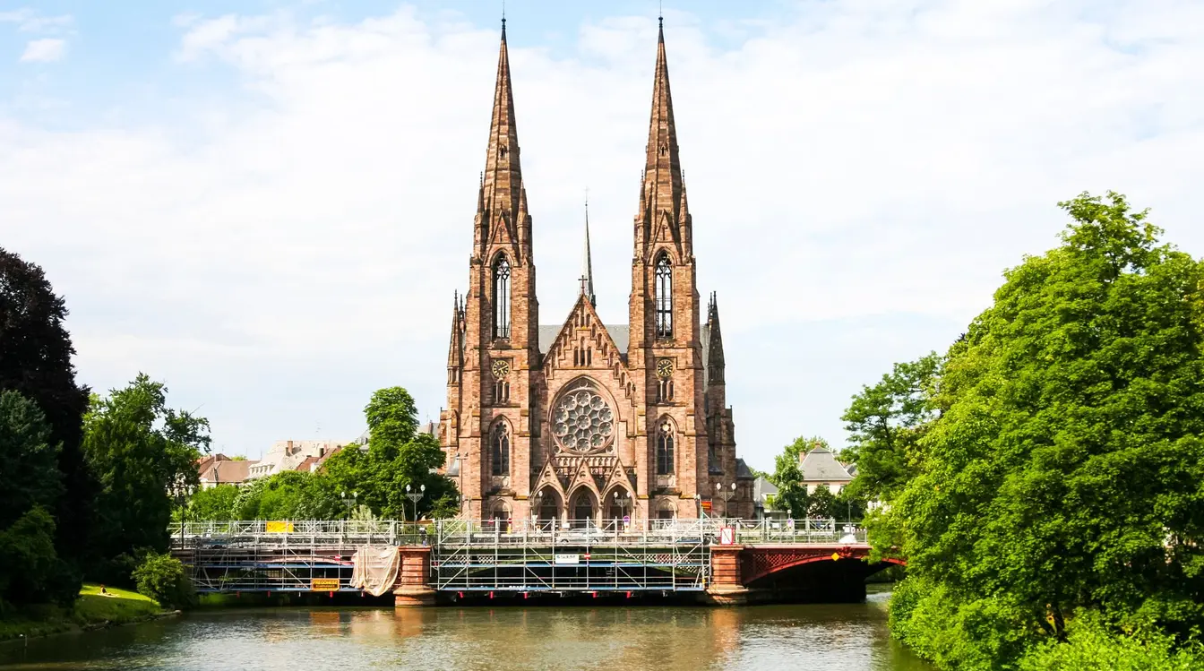 Strasbourg Cathedral in France, with green trees and river.