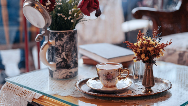 A photograph of the inside of a Viennese coffee house. It shows a table topped with a lace table cloth and a glass panel, on which there is a very pretty coffee cup and saucer decorated in gold and painted delicate flowers. There is coffee in the cup. To illustrate a blog post entitled 'Which Country Has the Best Coffee Culture?'