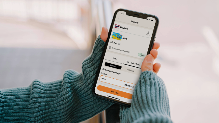 A colour photograph of a woman's hands holding a phone and looking at the Airalo eSIM app. She is wearing a blue jumper, the phone is back and the background is a pale pink colour. To illustrate a blog post entitled 'How to Add an eSIM to an Oppo Phone.'