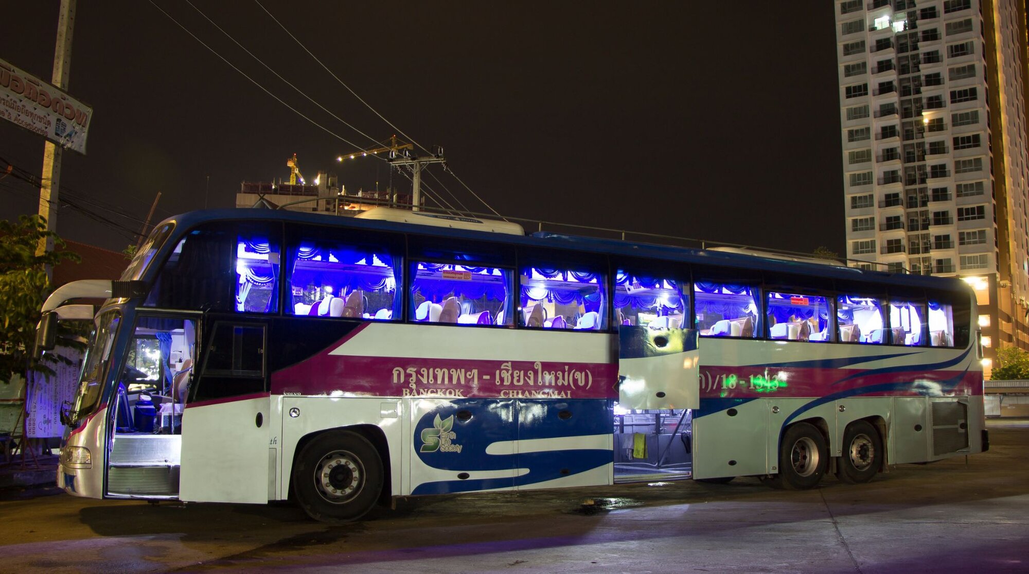 Side view of a long-distance passenger bus in Thailand with an open luggage compartment beneath the seating area.